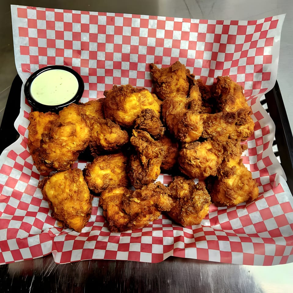 A basket of golden-brown fried chicken pieces with a side of creamy green dipping sauce.