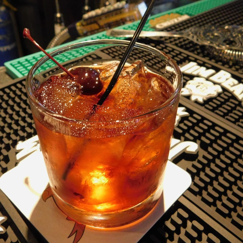 A refreshing cocktail with ice, a cherry, and a straw, on a bar mat at Crazy Craig's.