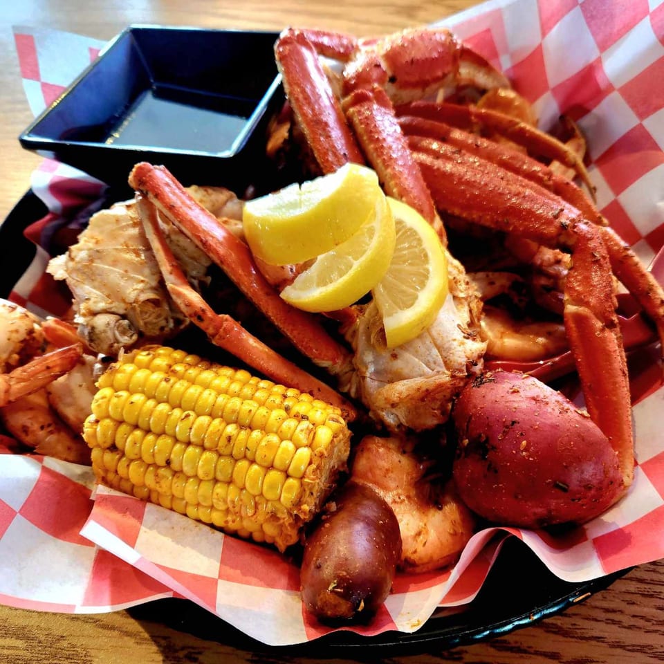 A seafood boil with crab legs, shrimp, corn on the cob, and potatoes in a basket.