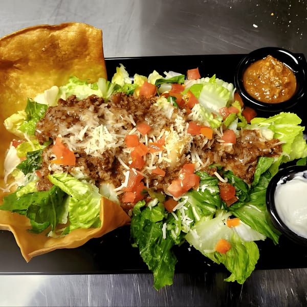A taco salad in a crispy tortilla bowl with ground beef, lettuce, tomatoes, cheese, salsa, and sour cream.