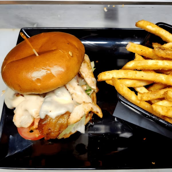 A chicken sandwich with melted cheese, lettuce, and tomato, served with a side of golden fries.