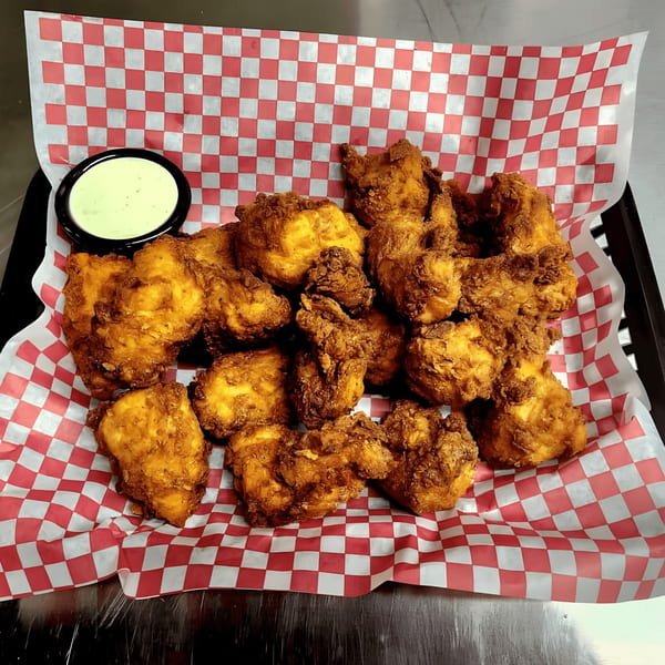 A basket of golden-brown fried chicken pieces with a side of creamy green dipping sauce.